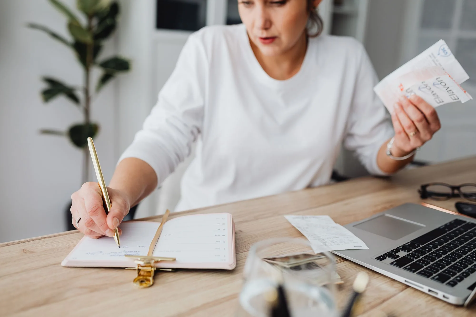 Persoon maakt aantekeningen in een agenda naast een laptop bij het plannen van de financiën